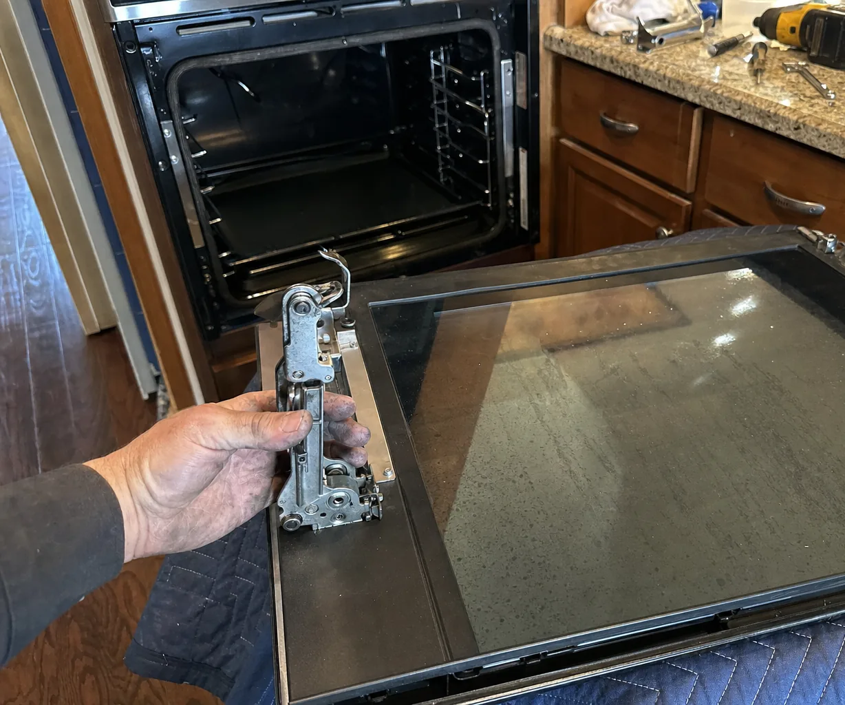 An oven door face-up on a blanket with its inner glass exposed and hand tools on the worktop above