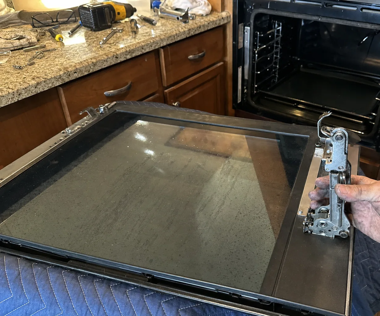 A removed appliance door resting on a padded blanket on a hardwood floor beside an open cabinet opening