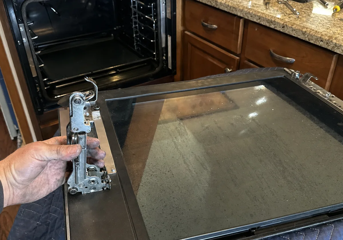 The empty opening of a built-in wall oven with the door removed and the hinge receivers visible at the sides