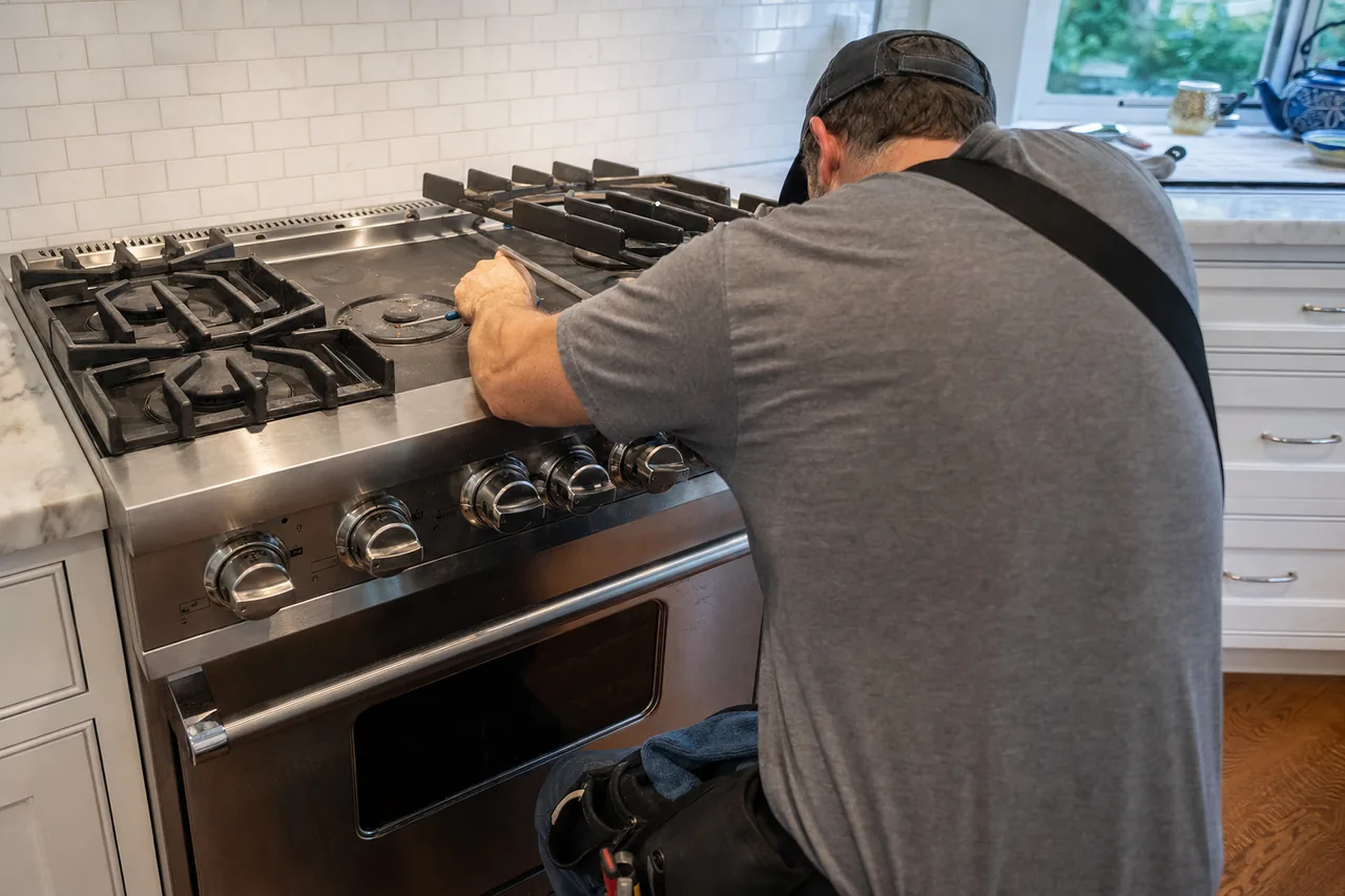 A stainless professional gas range set into marble counters, a technician leaning across the burners with a small tool